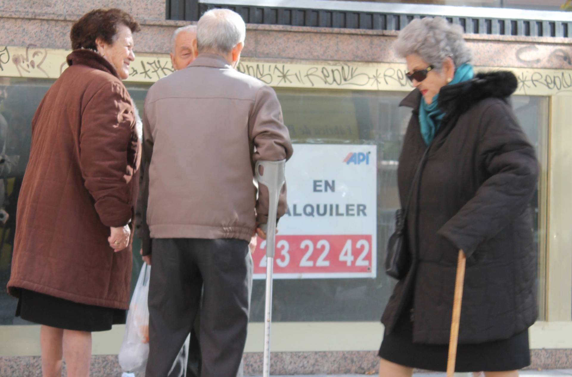 Grupo de personas mayores ante de un cartel de oferta inmobiliaria.