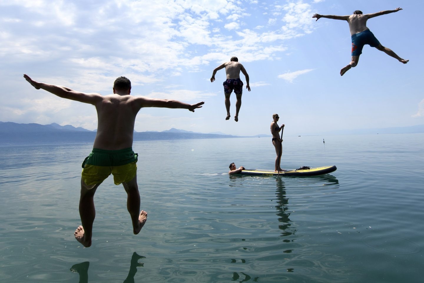 Varias personas disfrutan del buen tiempo en el lago de Lemán en frente de los Alpes.