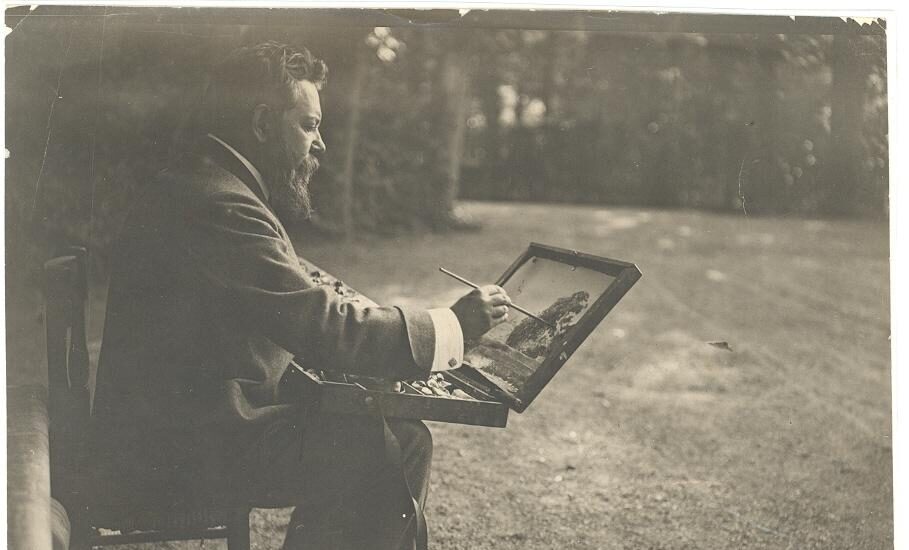 El pintor toma un apunte sentado, usando como caballete la tapa de su caja de pinturas, en los jardines de La Granja.