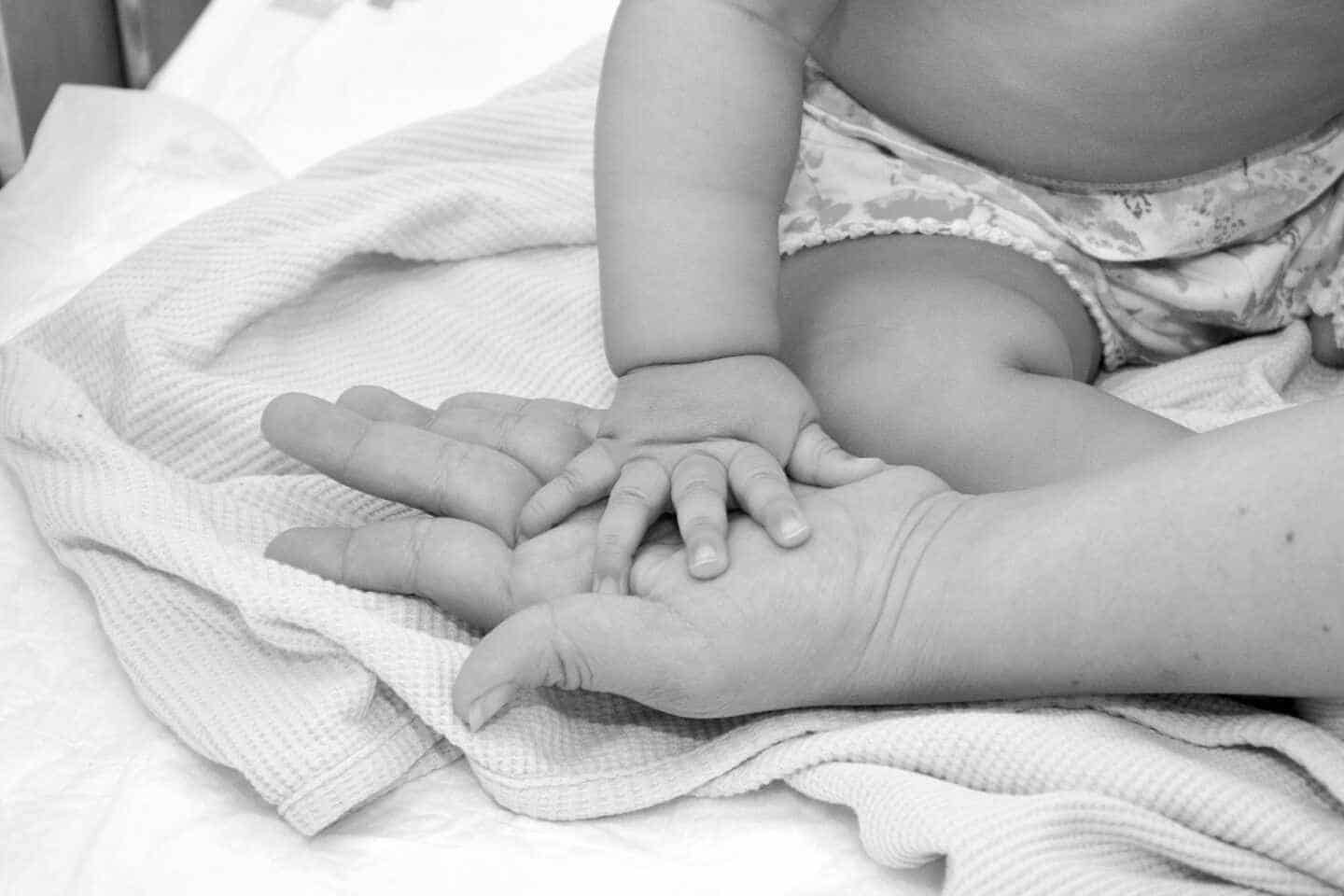La mano de un bebé sobre la mano de su madre en el Hospital Niño Jesús de Madrid, foto en blanco y negro