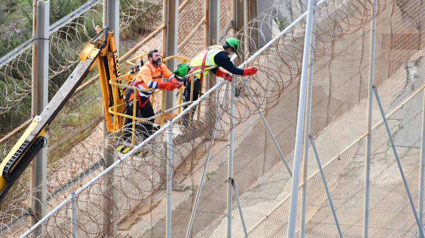 Dos operarios, trabajando en la retirada de las concertinas que coronan la valla fronteriza de Ceuta.
