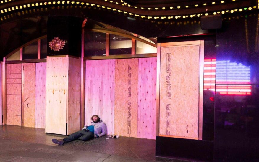 Un hombre duerme apoyado en un panel de madera colocado en el escaparate de una tienda en Nueva York para prevenir disturbios
