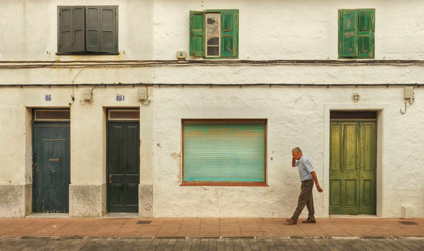 Un hombre de edad avanzada pasea frente a unas casas viejas.