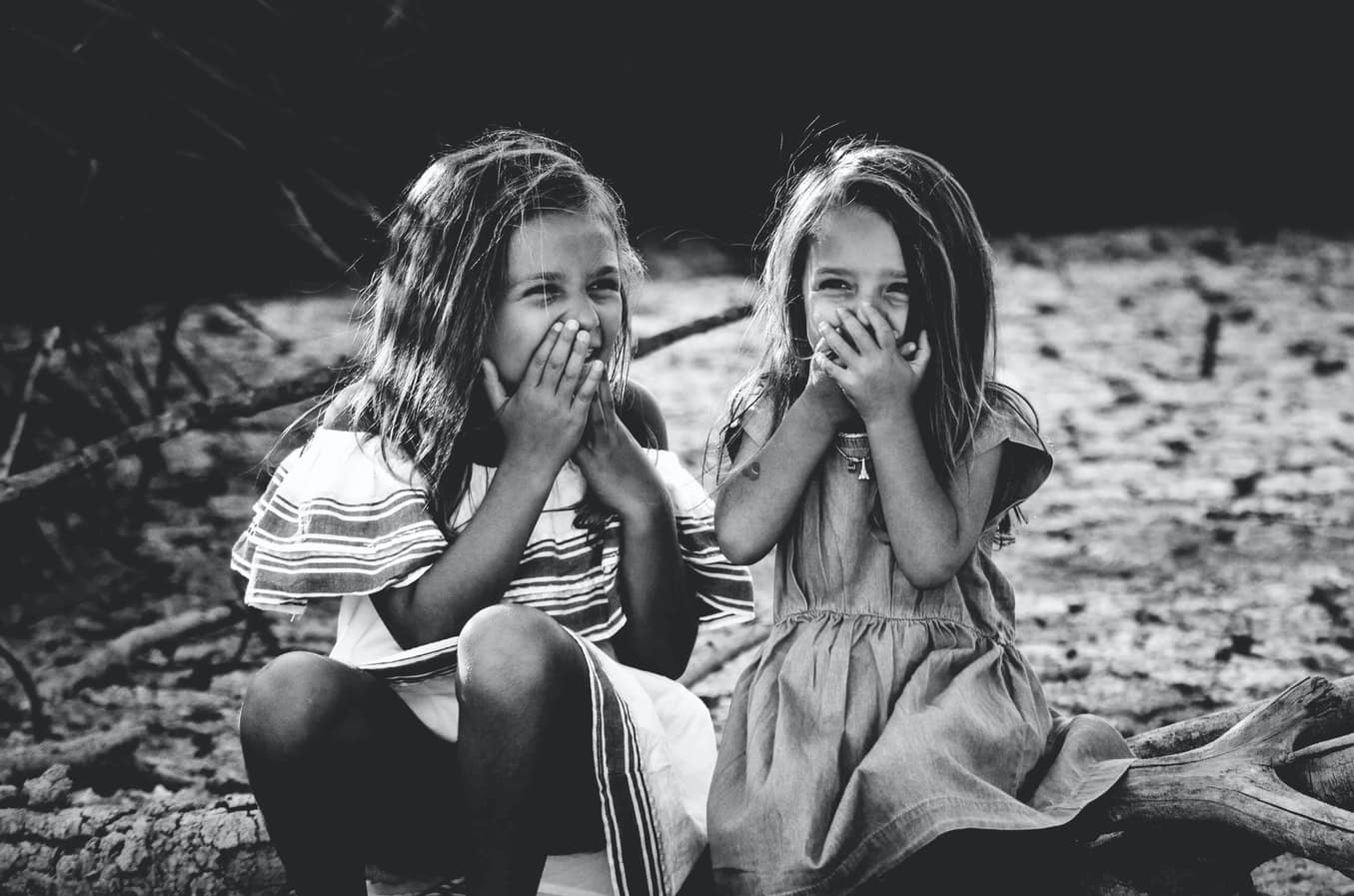 Dos niñas sonríen con las manos en la boca.