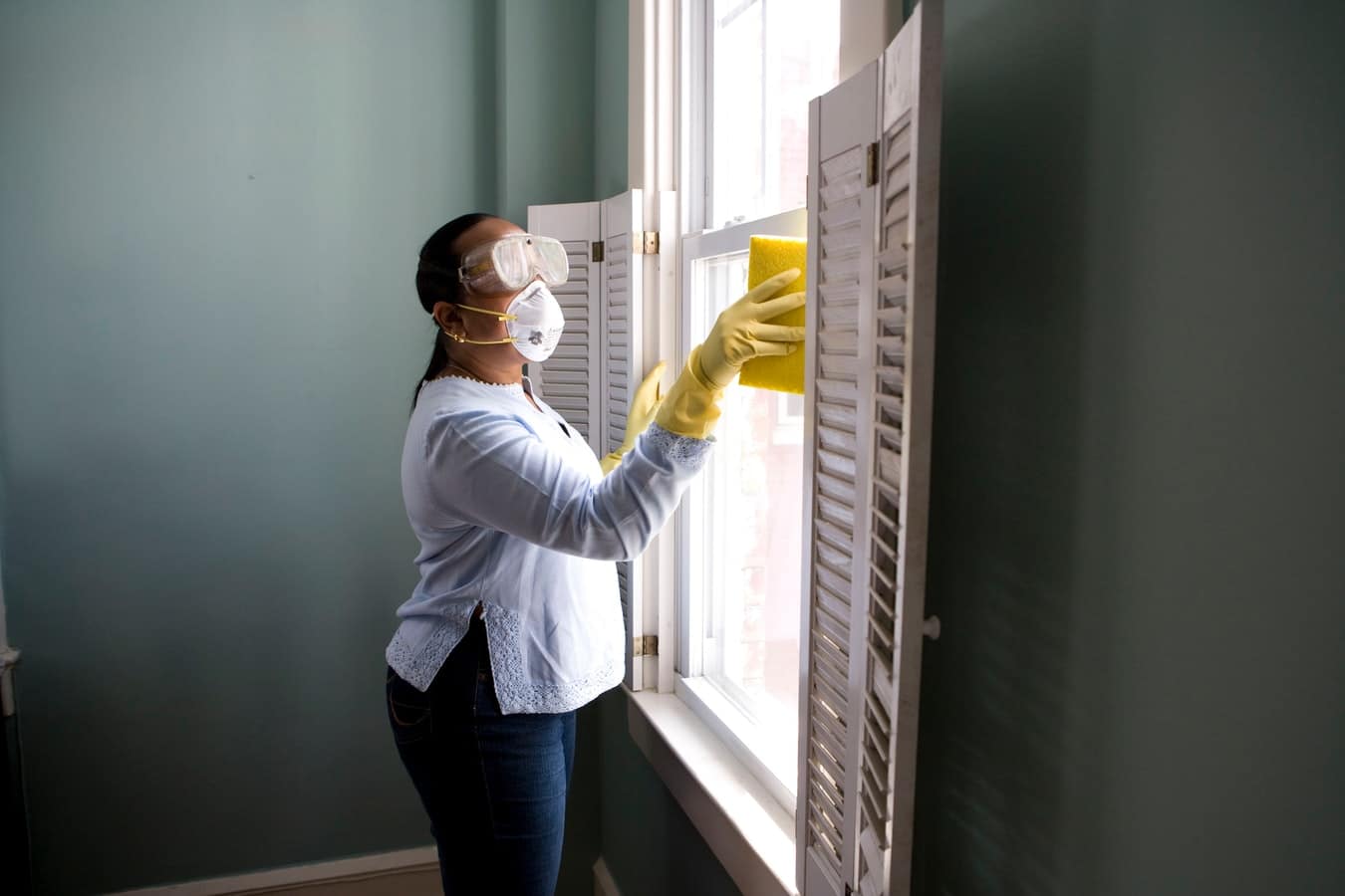 Una mujer limpia una casa equipada con mascarilla y gafas puestas.