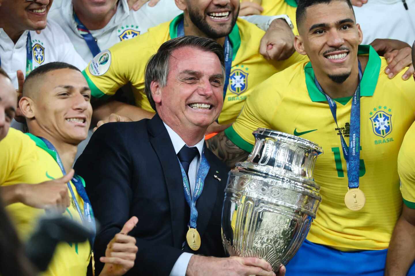 El presidente de Brasil, Jair Bolsonaro, sostiene la Copa América de 2019, rodeado de la selección nacional