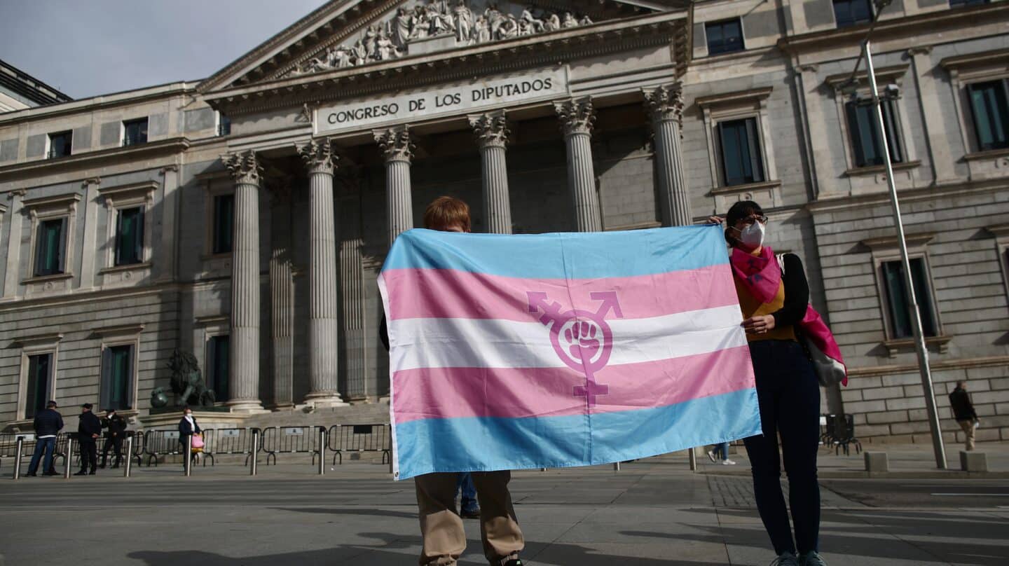 Dos personas sostienen una bandera trans durante una concentración convocada frente al Congreso.