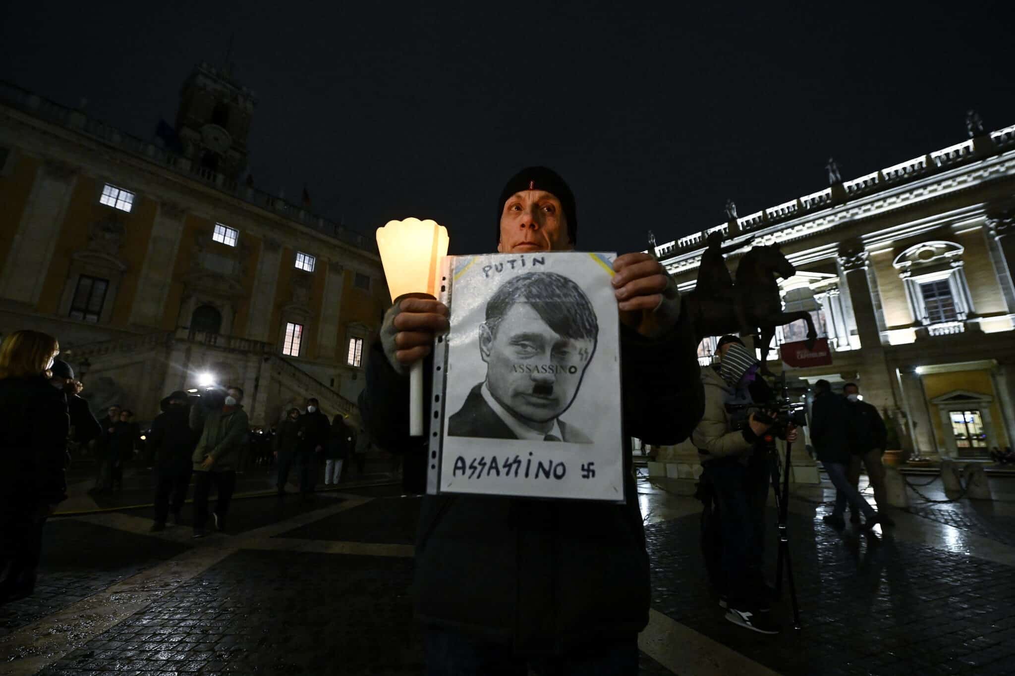 Un hombre muestra un cartel en el que se ve a Putin como si fuera Hitler en una manifestación en Roma