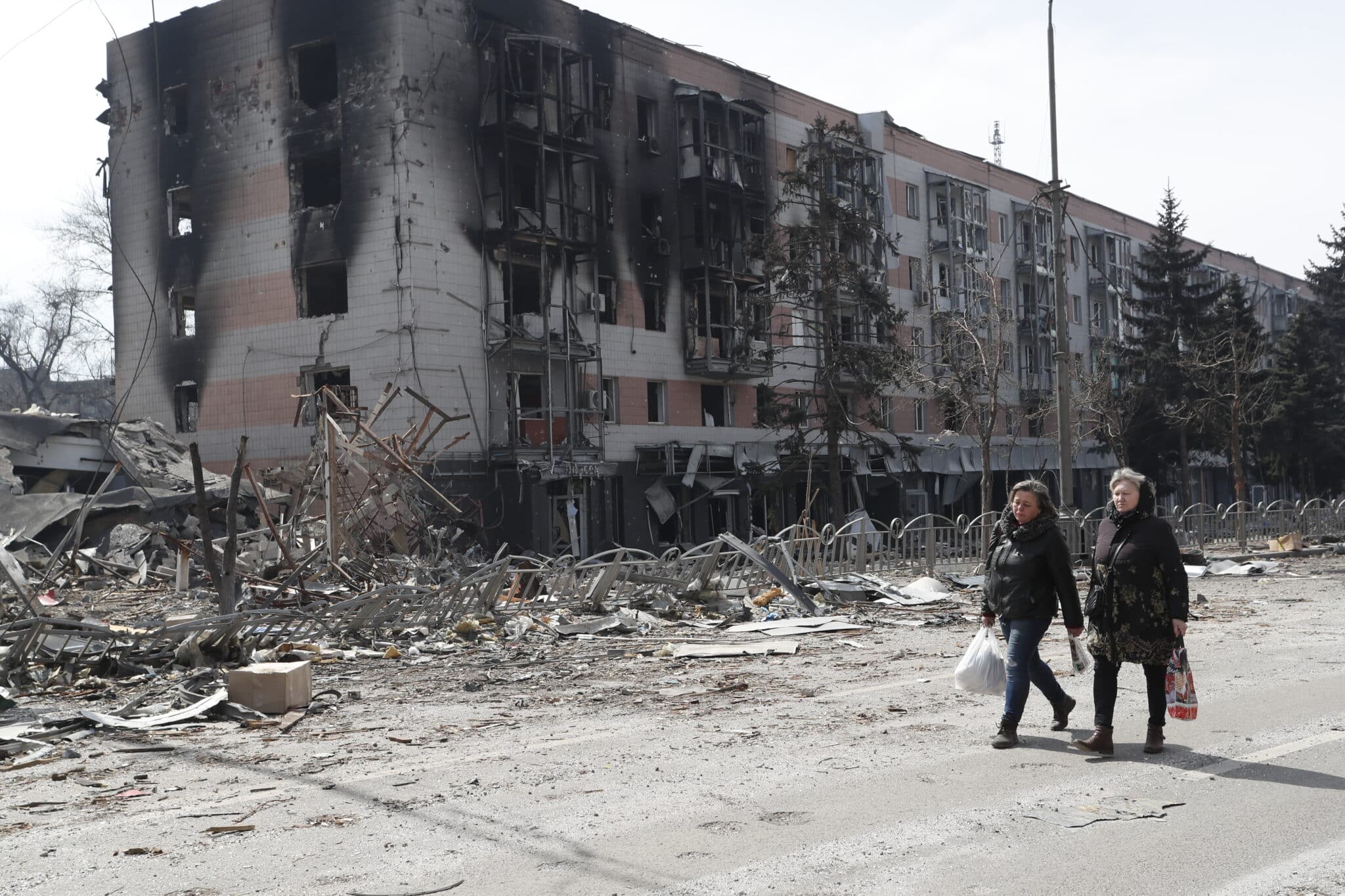 Dos mujeres caminan frente a un edificio destruido en Mariúpol.