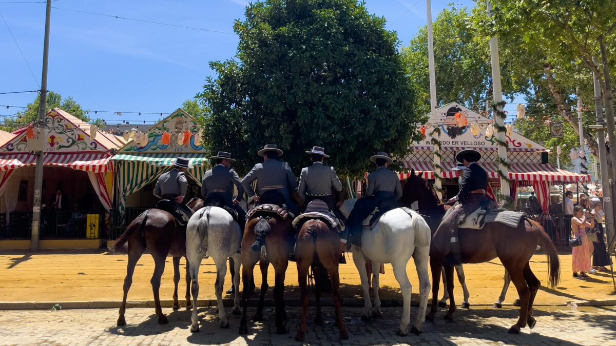 Un grupo de caballistas se refugian junto a la sombra de un naranjo en el Real de la Feria de Abril de Sevilla, donde se esperan temperaturas de cerca de 35 grados debido a una ola de calor.