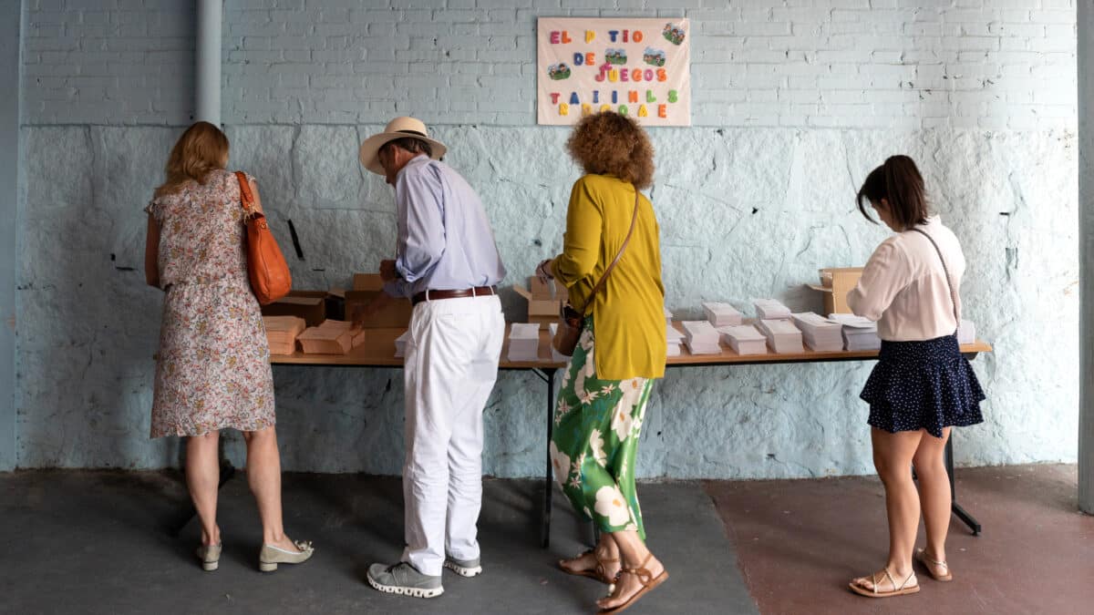 Varias personas cogen papeletas para ejercer su derecho a voto durante las elecciones generales, en el Colegio Ramiro de Maeztu, a 23 de julio de 2023-