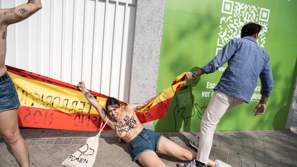 Una persona trata de impedir una protesta del colectivo activista FEMEN frente a la sede nacional de Vox