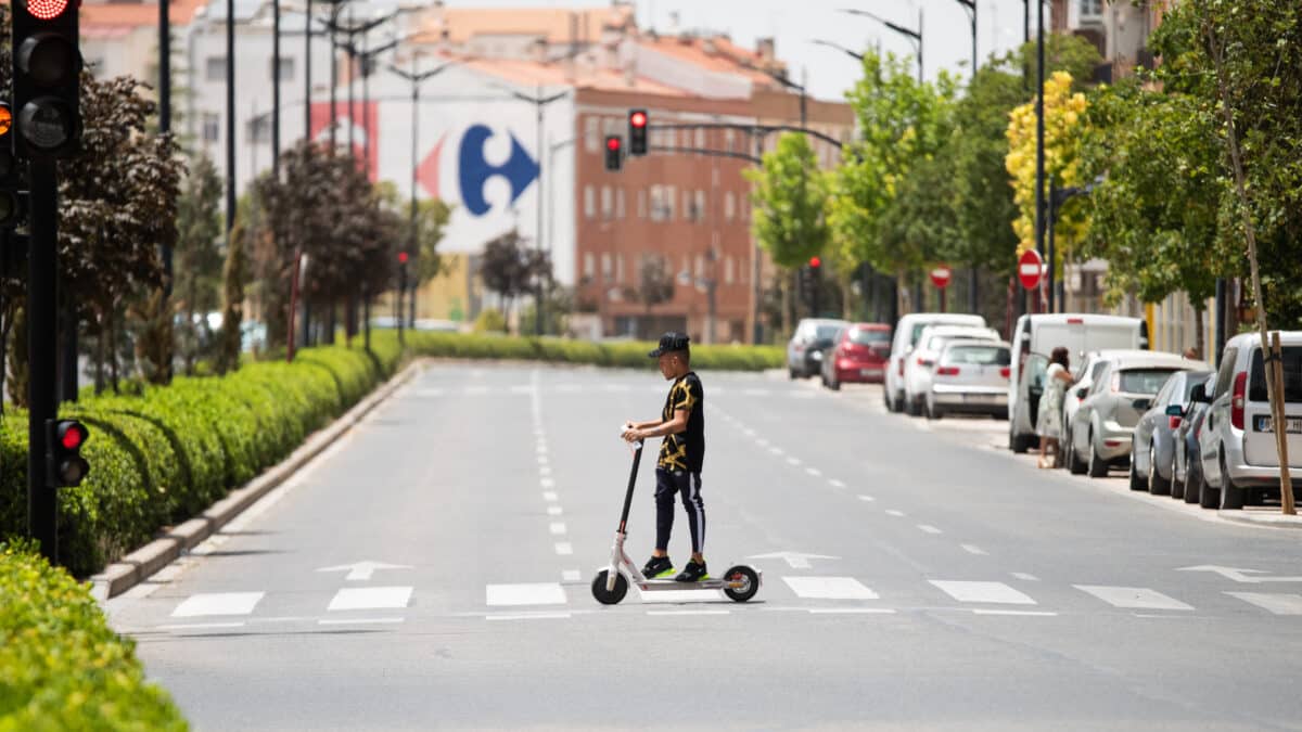 Un joven cruza con un patinete eléctrico bajo el sol en la Calle Hellín, a 11 de julio de 2023