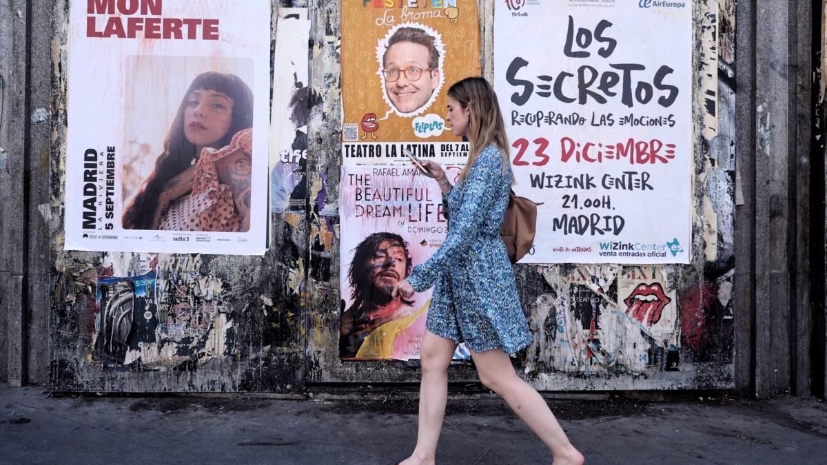 Una joven pasa delante de varios carteles de conciertos en Madrid.