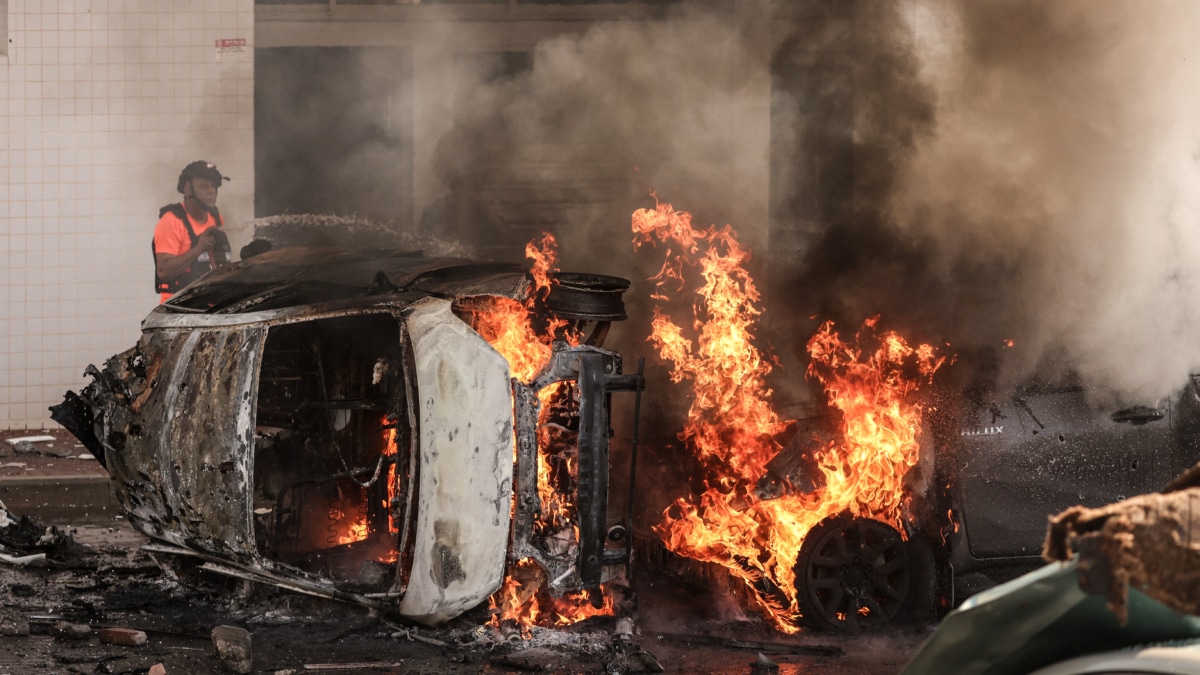 Varios vecinos de Ashkelon intentan apagar el fuego de un vehículo tras el ataque de Hamás.