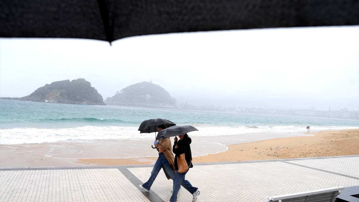 Dos mujeres caminan con paraguas en la playa de Ondarreta.