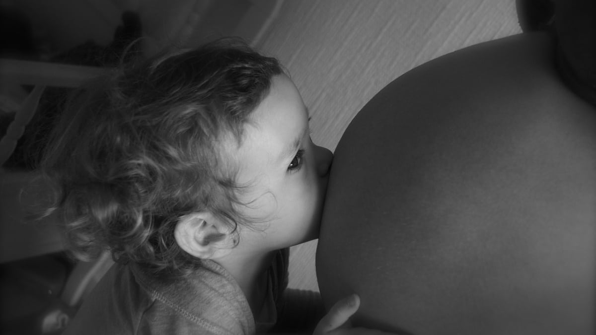 Un bebé besa una barriga de embarazada.