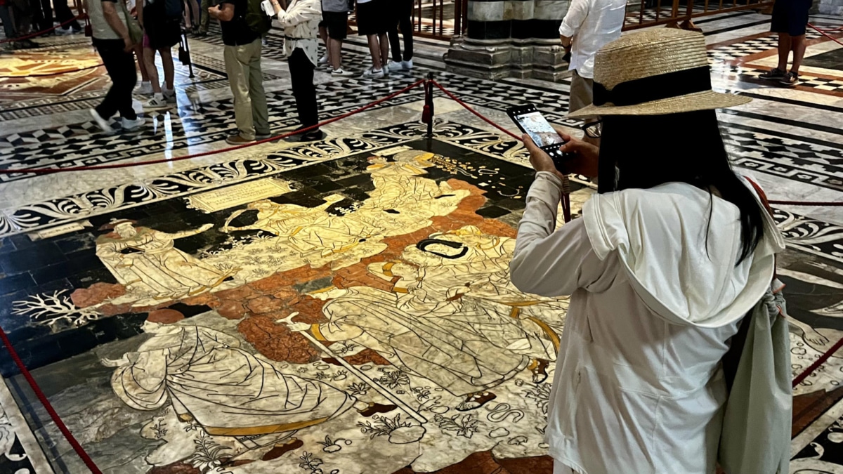 Visitantes de la catedral de Siena observan las decenas de mosaicos y escenas que decoran el pavimento del templo.