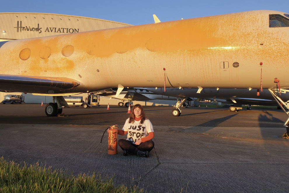 Una activista de Just Stop Oil posa frente a un jet privado que fue rociado con extintores llenos de pintura naranja en el aeródromo Stansted, donde poco antes aterrizó el jet privado de la artista Taylor Swift. 