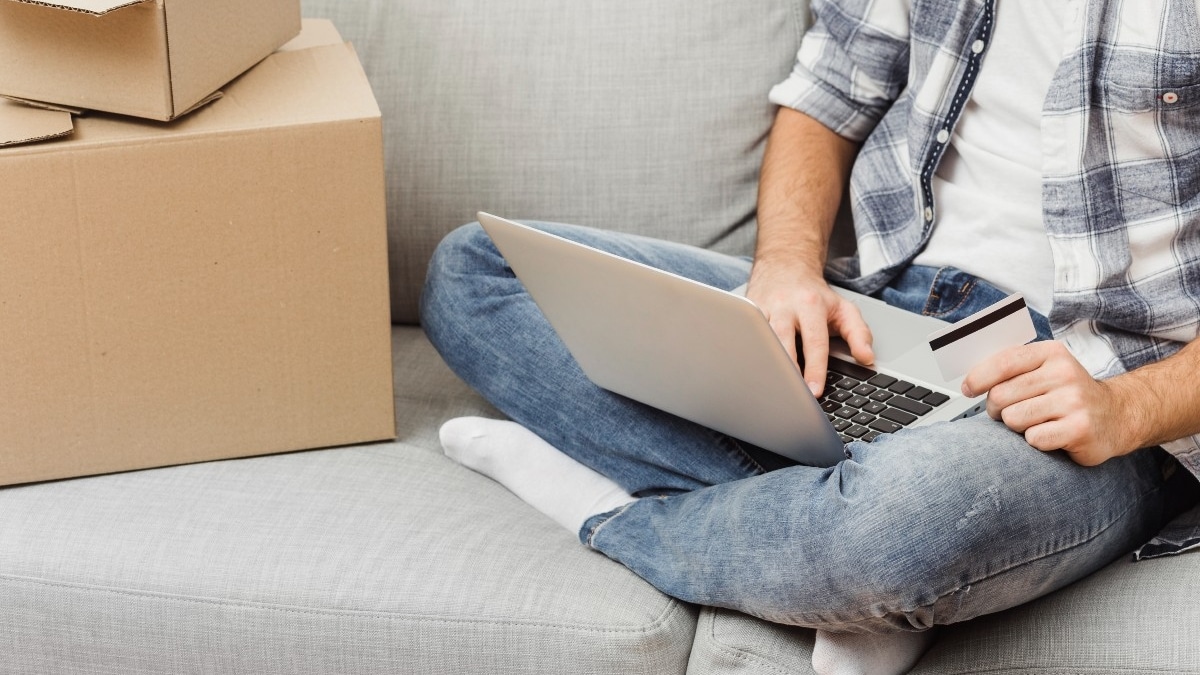 Hombre sentado comprando por internet con cajas de envíos al lado