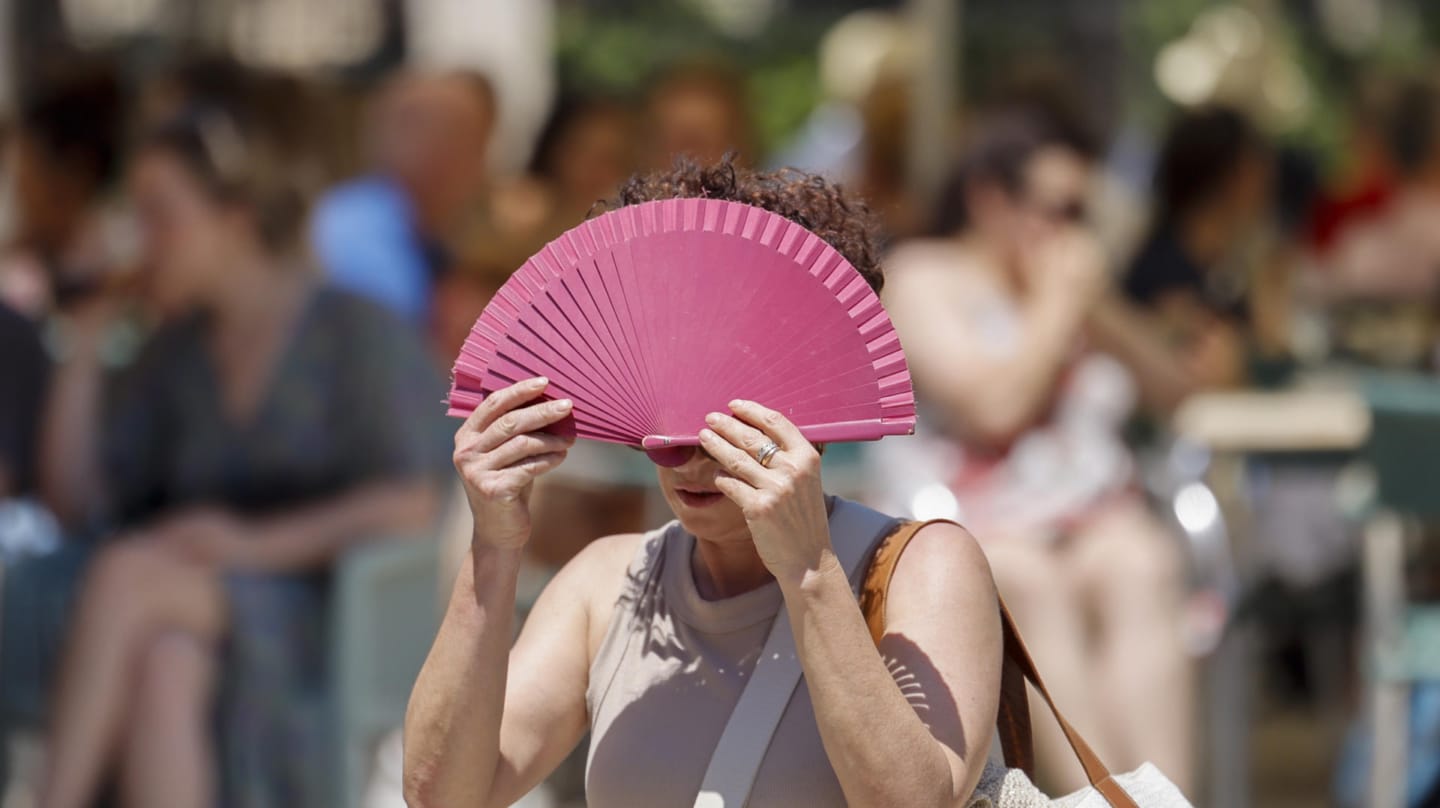 Una mujer se protege con un abanico del sol y del calor.