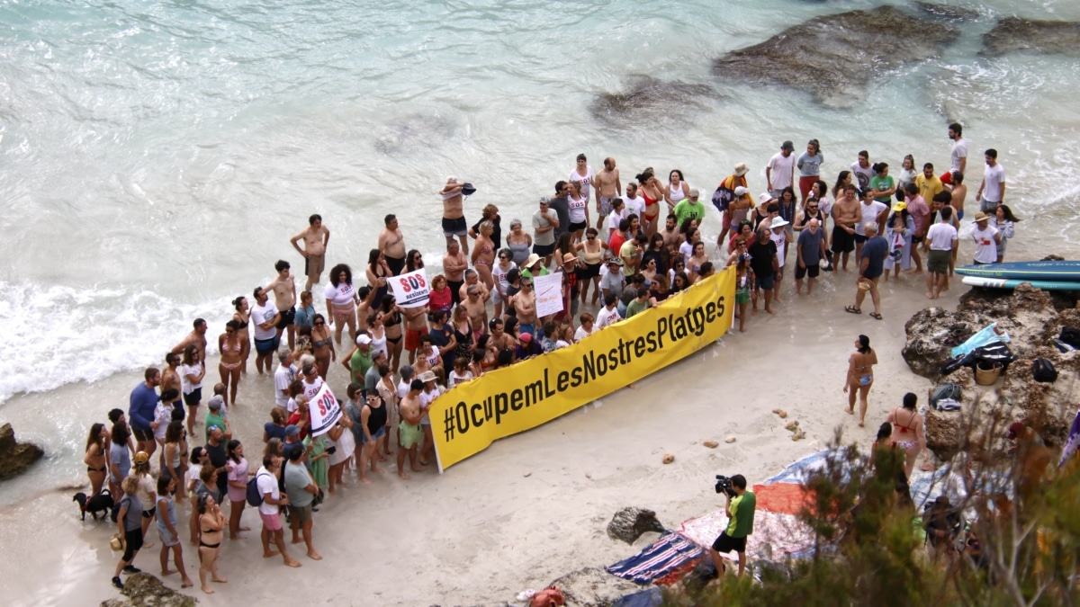 Varias personas junto a una pancarta durante la protesta contra la masificación turística en el Caló des Moro, este domingo.