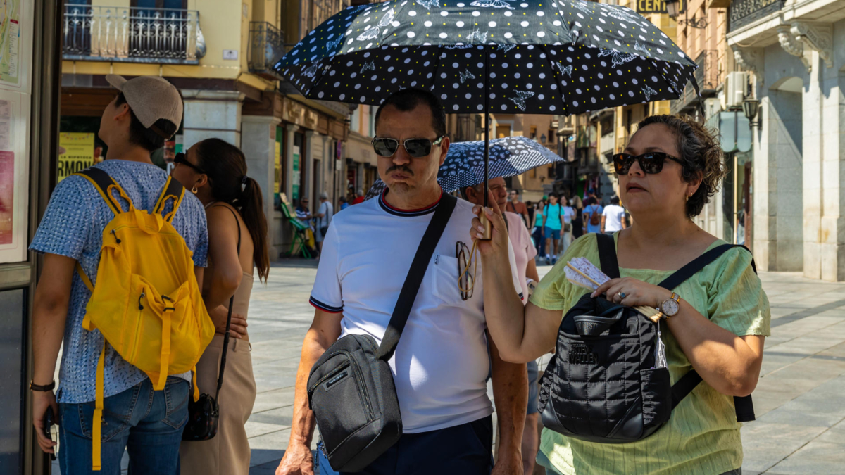 Unos turistas se protegen del calor con una sombrilla en Toledo