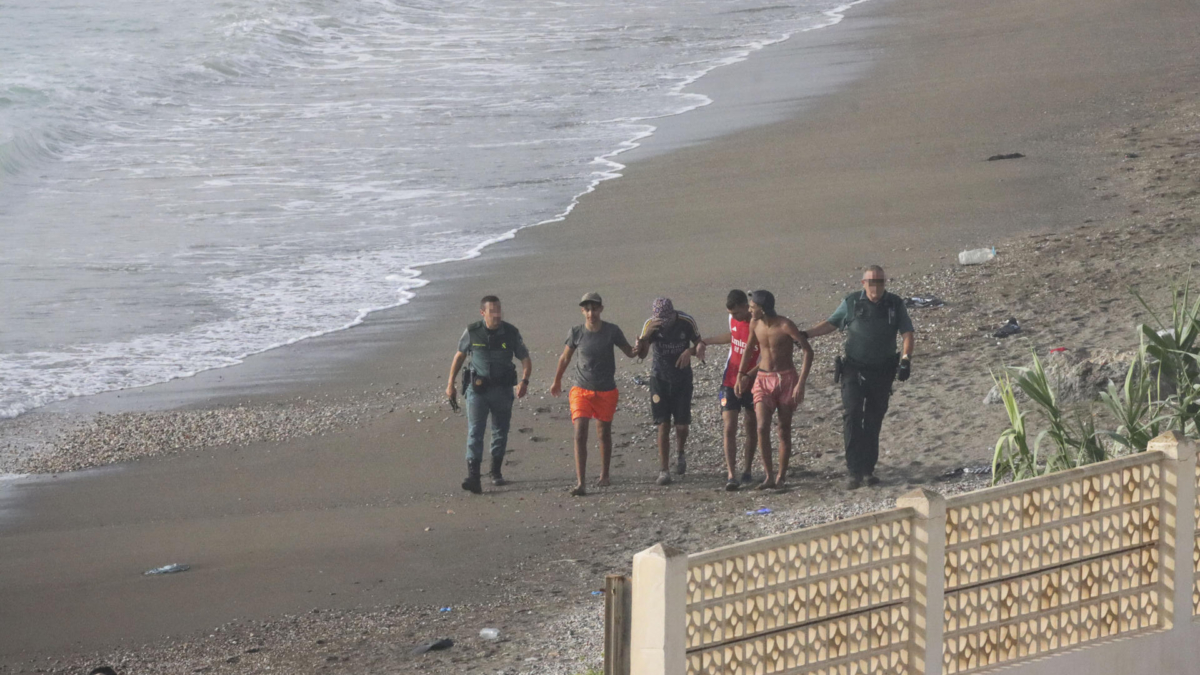 Personas migrantes en la playa de Ceuta acompañadas por miembros de la Guardia CIvil.