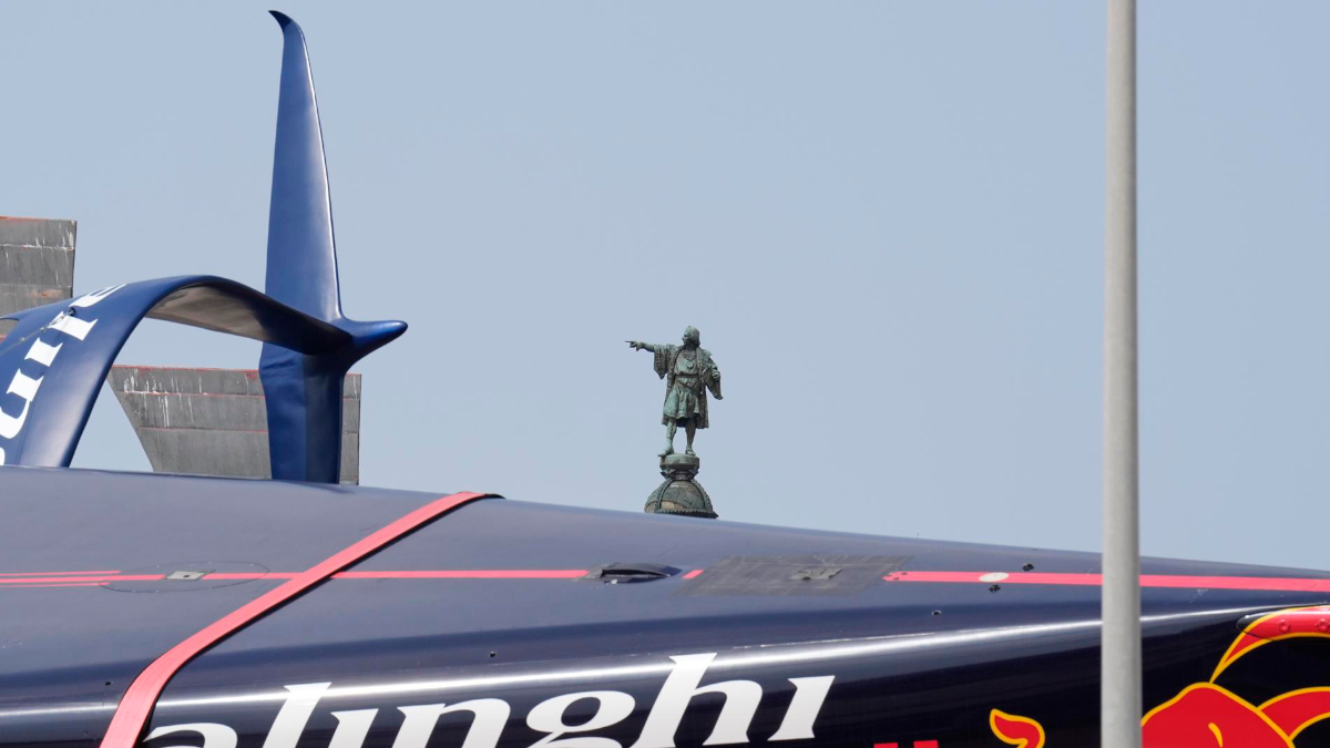 El casco del Alinghi, uno de los veleros que participan en la Copa América de Vela, con el monumento a Colón de Barcelona al fondo.