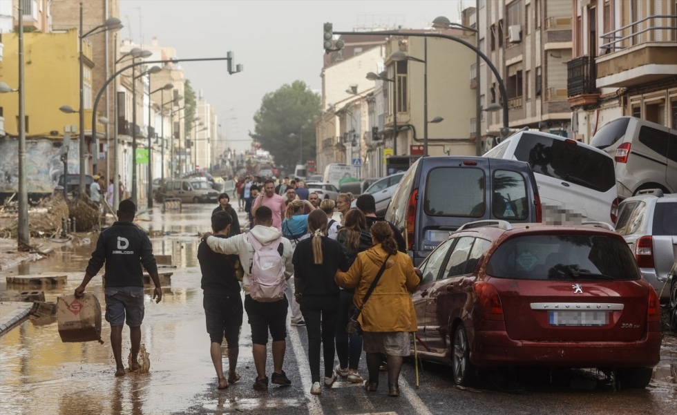 Varias personas junto a coches destrozados tras el paso de la DANA por el barrio de La Torre de Valencia