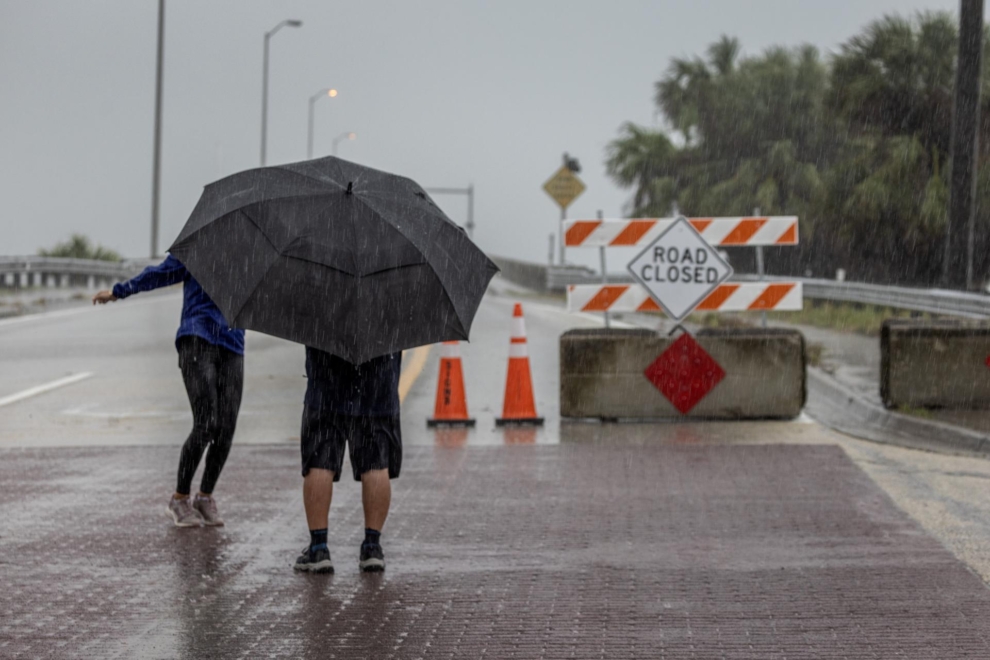 Dos personas frente a una señal de carretera cortada en Oyster Bay, Sarasota, mientras Florida se prepara para la llegada del huracán Milton.