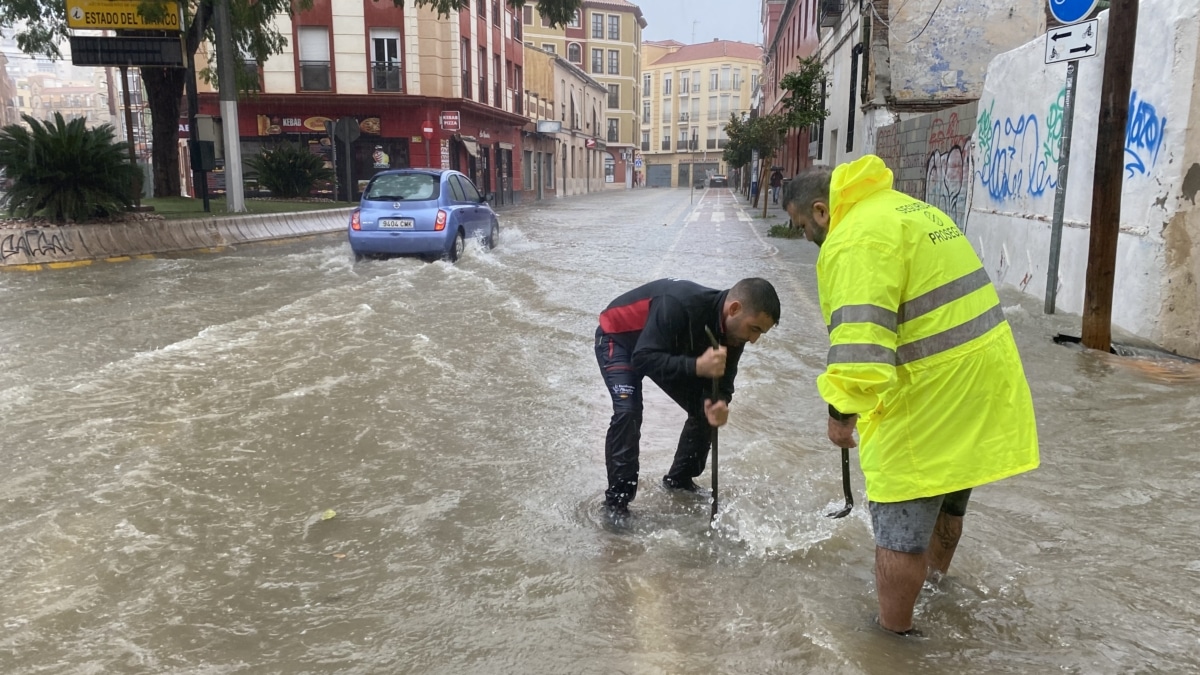 Varias personas intenta levantar la tapa de una alcantarilla en una calle inundada de agua debido a las fuertes lluvias