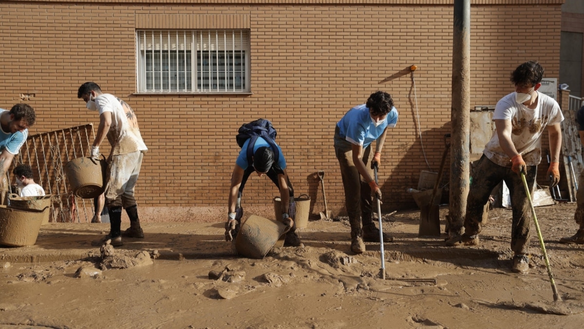 Varios jóvenes trabajan para despejar una calle de Paiporta en los primeros días tras la DANA que asoló Valencia.