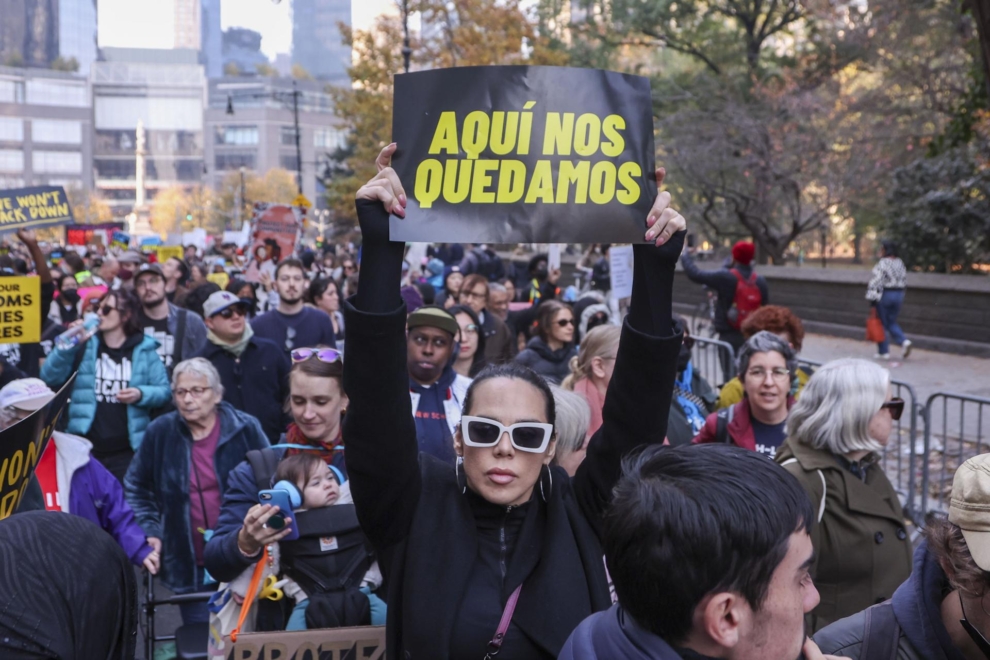 Una mujer lleva una pancarta en la que se lee 'Aquí nos quedamos', en una manifestación contra Trump en Nueva York.