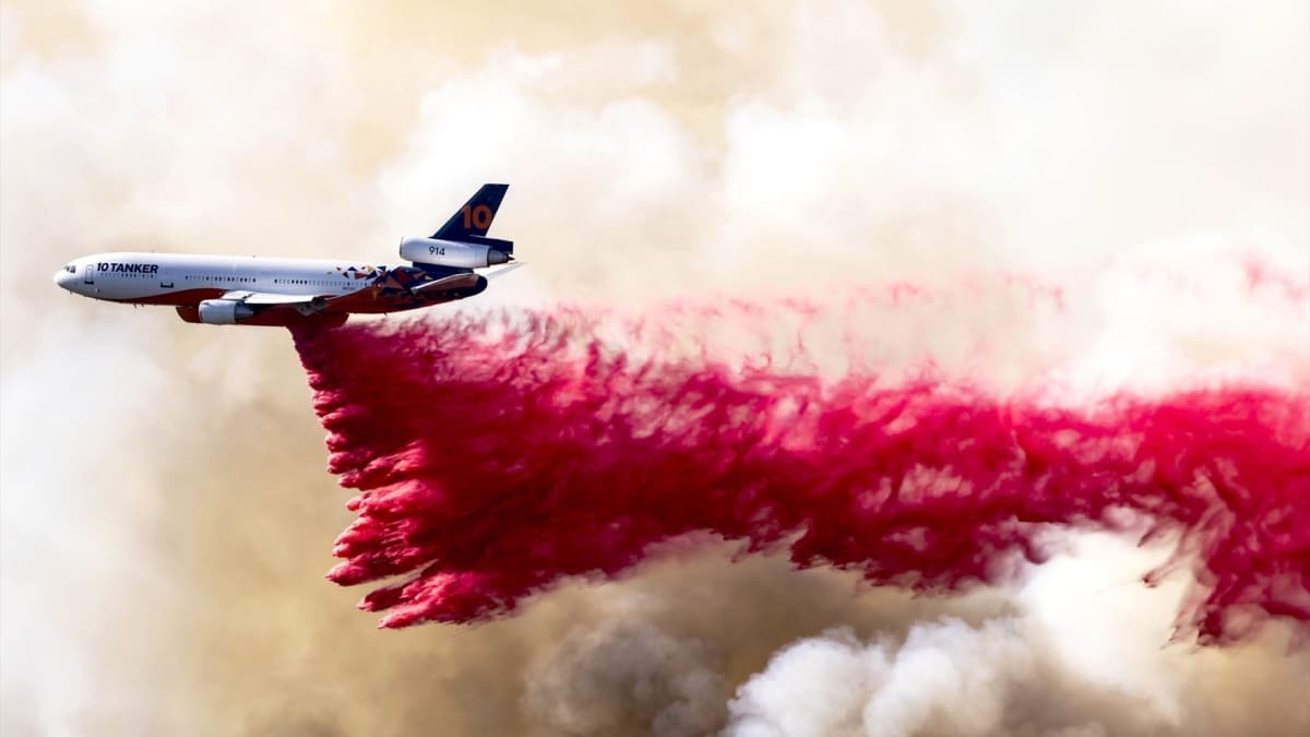 Un avión arrojan do líquido rojo para apagar un incendio.