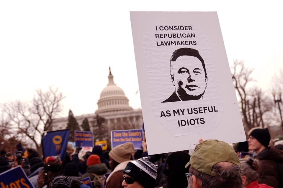 Manifestantes se reúnen en una concentración organizada por un sindicato de funcionarios (AFGE) a las puertas del Capitolio, en Washington. En la pancarta se lee "Considero a los legisladores republicanos como mis idiotas útiles", junto a una imagen de Elon Musk.