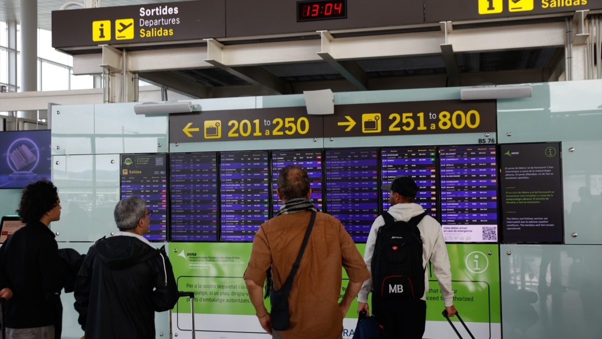 Varias personas miran los paneles informativos en el aeropuerto de Barcelona-El Prat.